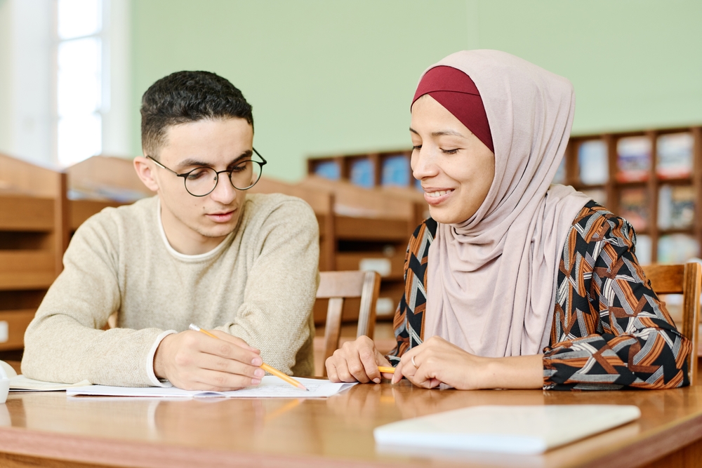Young,Man,And,Woman,In,Hijab,Sitting,At,Desk,In